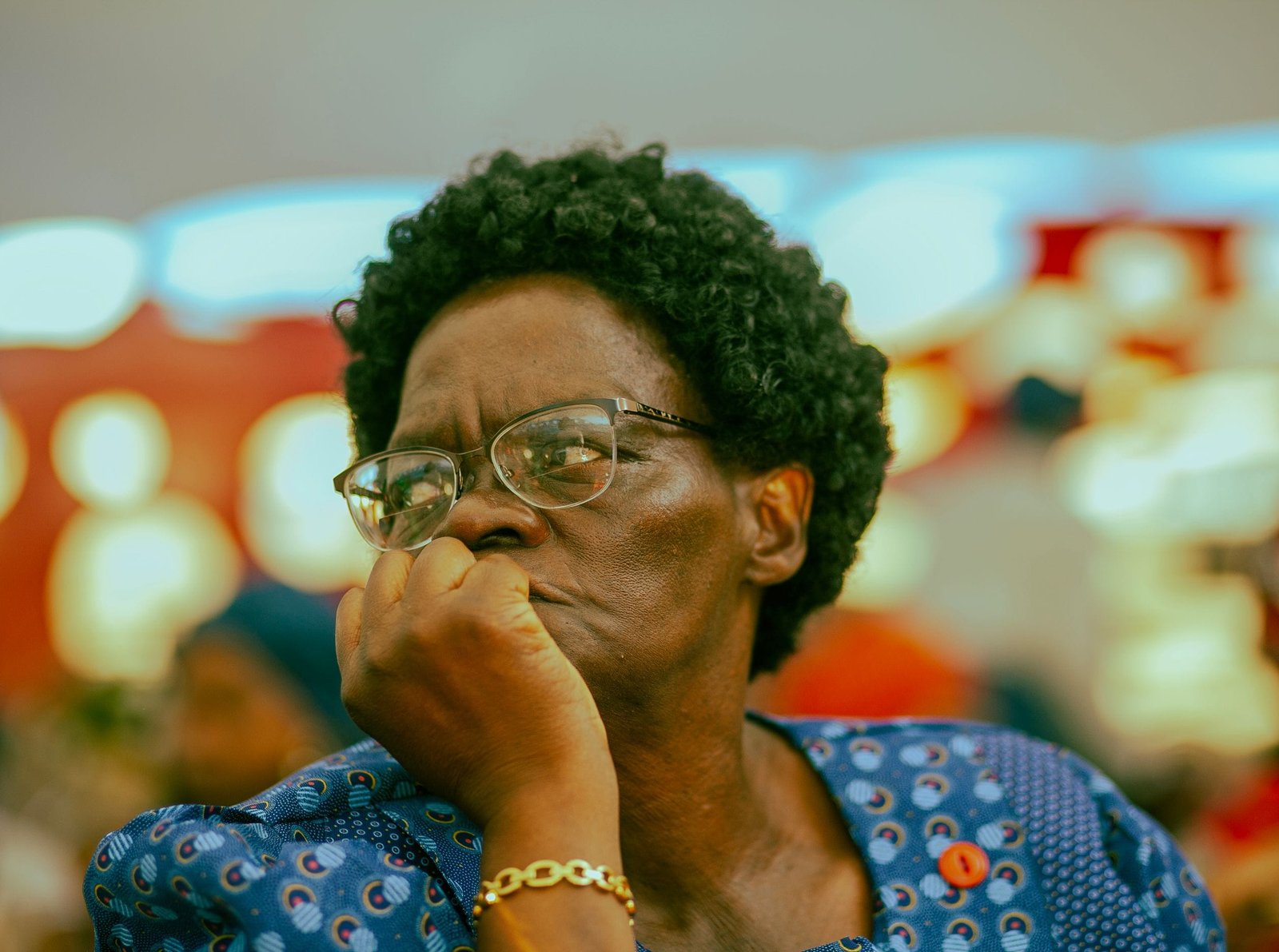 Elderly woman in Soweto deep in thought, wearing glasses and blue attire.